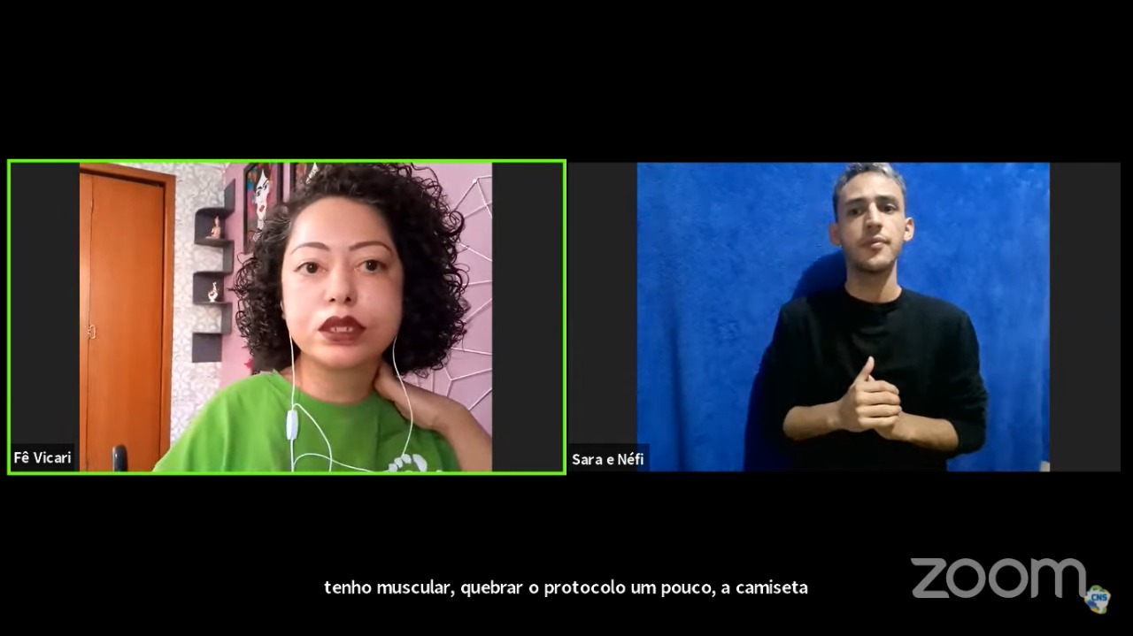 #PraCegoVer #PraTodosVerem #PraTodoMundoVer: A imagem é um print da live onde aparecem duas telas. Na esquerda está Fernanda Vicari, vestida de verde, e na direita o intérprete Nefi, vestido de preto.